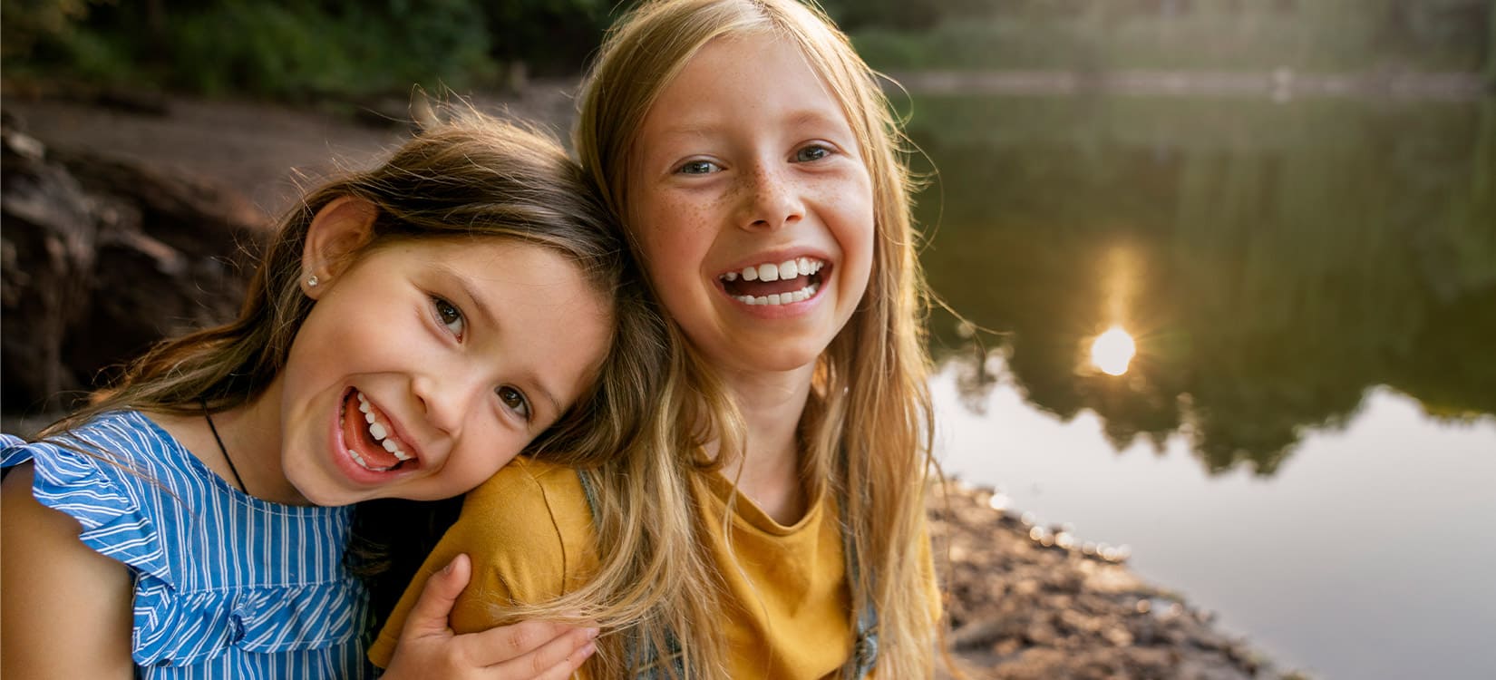 Zwei Mädchen lachen im Sonnenschein am Wasser.