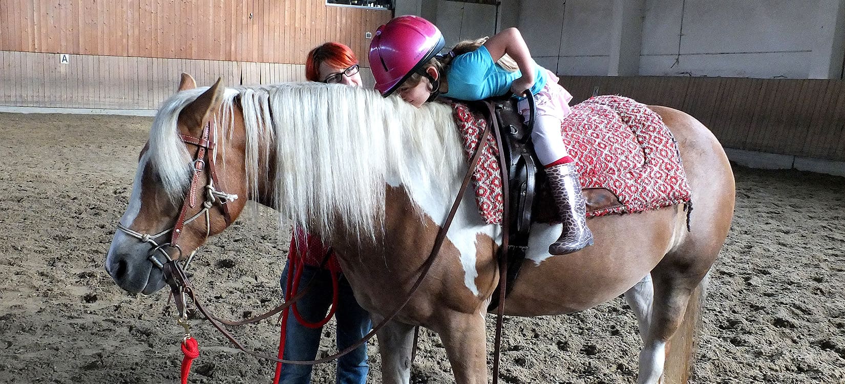 Reitpädagogin hilft Mädchen auf Pferd.