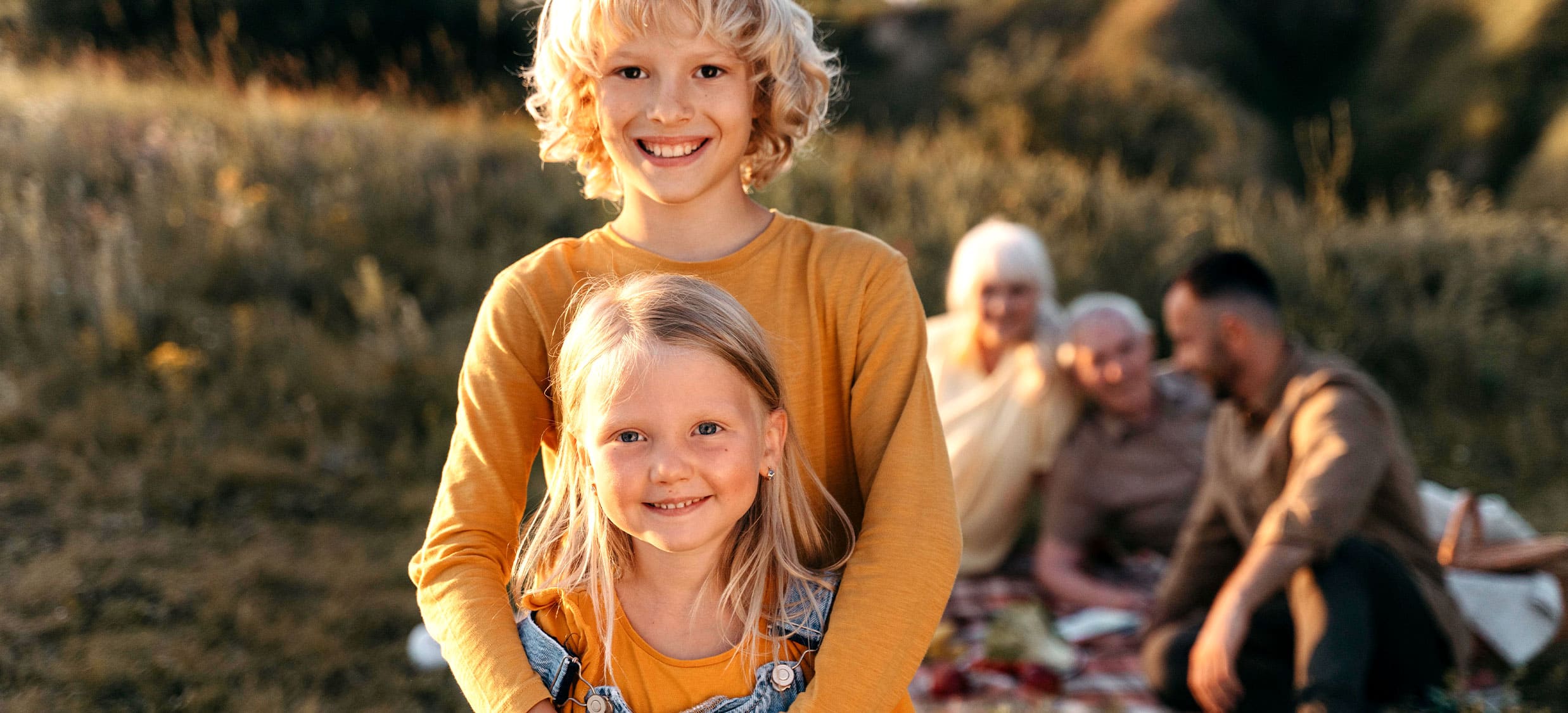 Kinder lächeln in der Natur. Großeltern und Vater picknicken im Hintergrund.